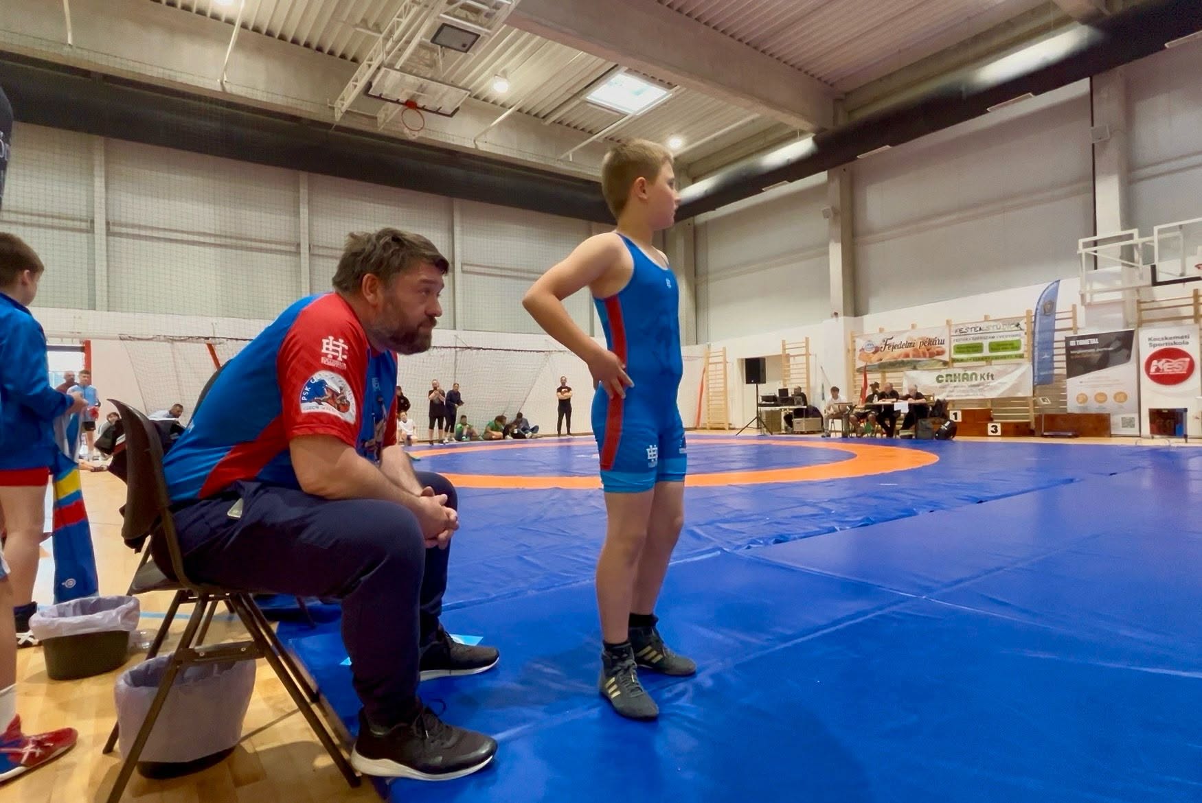 Trenér PSK Olymp Praha koučuje mladého zápasníka u žíněnky